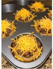 Onion rings filled with cooked ground beef and topped with shredded cheddar cheese in a muffin tin